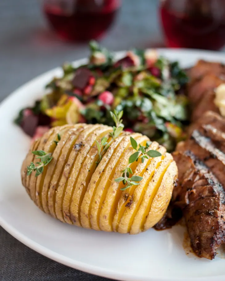 A hasselback potato on a plate with slicedsteak