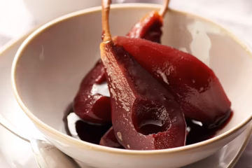A quartered pear poached in red wine in a dessert bowl.