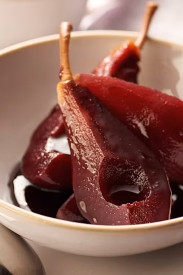 A quartered pear poached in red wine in a dessert bowl.