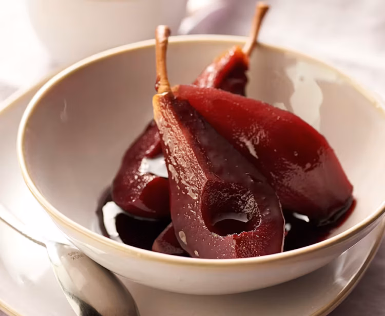 A quartered pear poached in red wine in a dessert bowl.