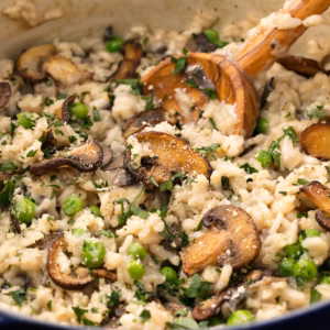 mushroom risotto being stirred with a wooden spoon